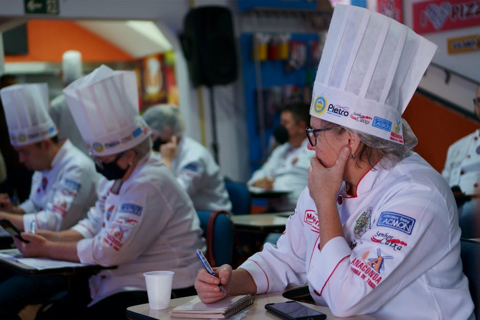 Group of chefs in a culinary class, attentively taking notes while wearing traditional hats and uniforms