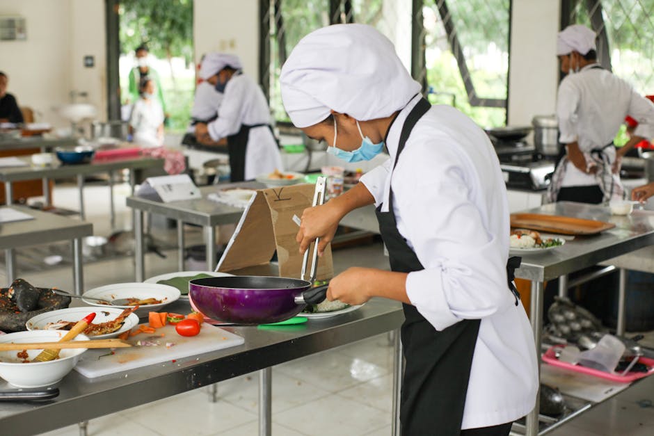 Culinary students in uniforms practice cooking skills in a professional kitchen setting