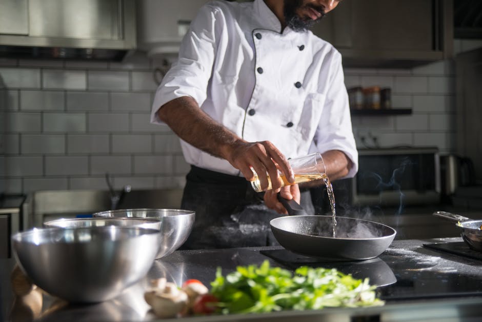 Chef in a professional kitchen pouring oil into a frying pan for cooking