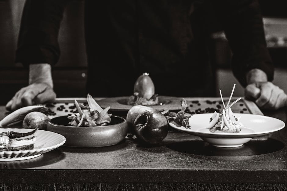 Chef arranges gourmet dishes on a table in a black and white setting