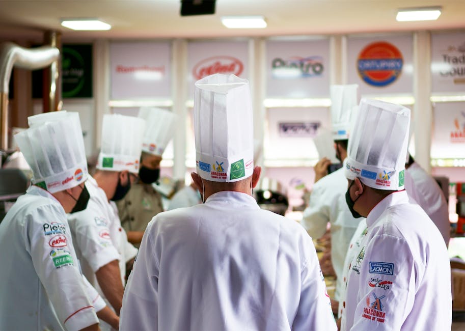 A group of professional chefs in white uniforms and hats working together in a busy commercial kitchen