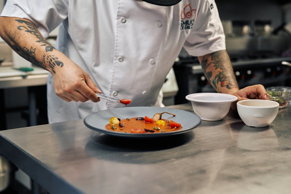 Tattooed chef garnishing a gourmet dish in a professional kitchen setting