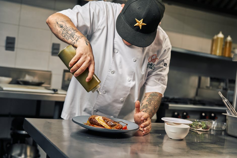 Chef garnishing a gourmet dish with sauce in a professional kitchen setting